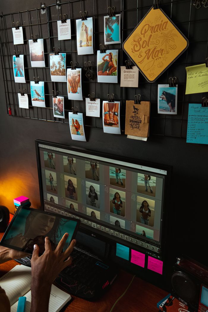 gallery-1 Photographer reviewing and editing images with a computer monitor and hanging photos on a wire grid.