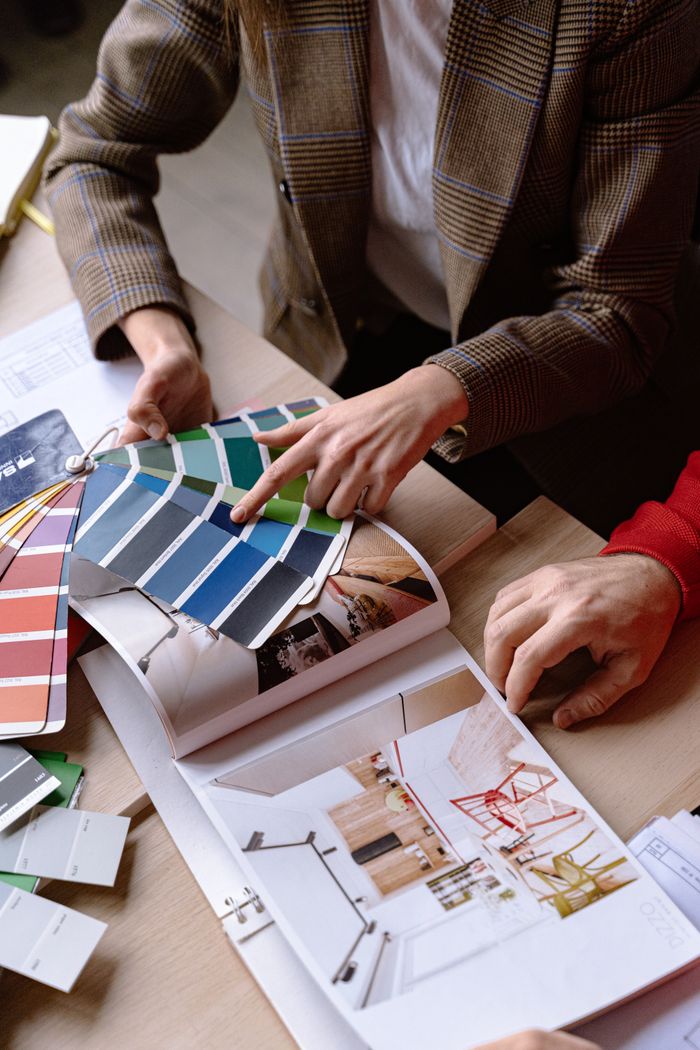 gallery-2 Interior designers discuss color swatches and design ideas at a table, planning a creative project.