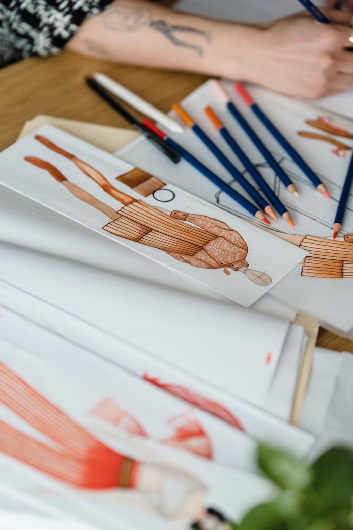 services-img From above of crop anonymous female designer at desk with pencils drawing against illustrations of human figures in outfit