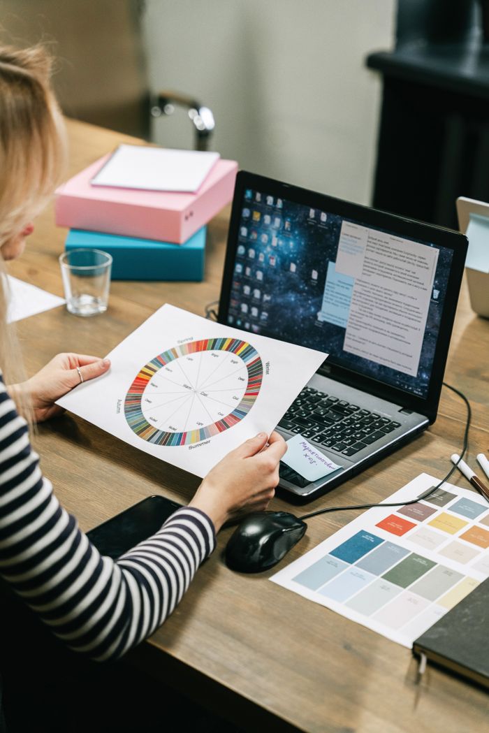 services-02 Businesswoman reviews color wheel and strategy documents on a laptop in an office setting.